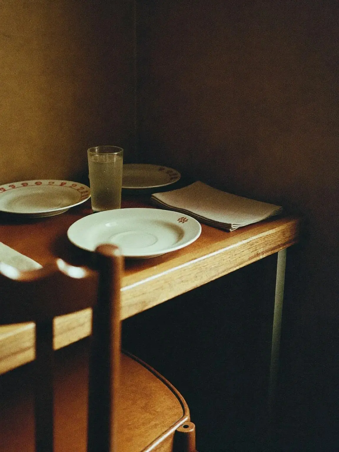 A laid table in the corner of the dining room, plain white plates under warm low light.