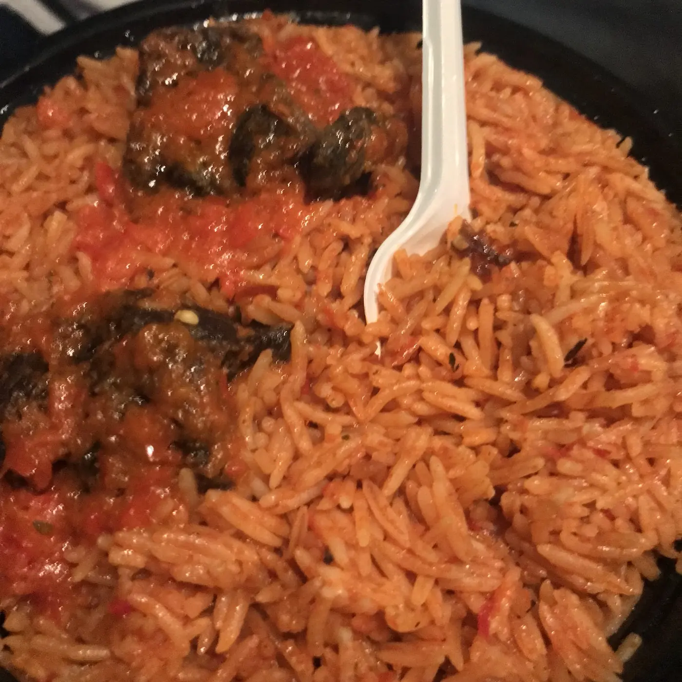 A pan of jollof rice in tomato sauce with pieces of stewed meat and a serving spoon, shot from above.